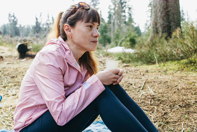 Young beautiful woman drinking hot tea or coffee from a thermos in the forest on a walk. hiking
