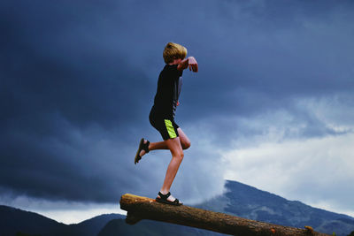 Low angle view of boy standing on mountain against sky