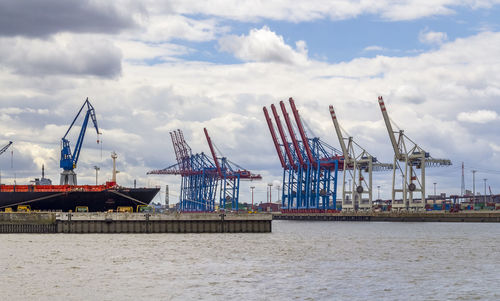 Cranes at commercial dock against sky