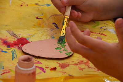 Cropped hand of girl painting wooden egg on yellow plastic