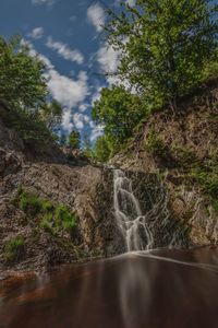 Water flowing over river in forest against sky
