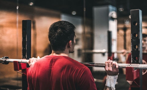 Rear view of man lifting barbell at gym
