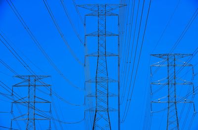 Low angle view of electricity pylon against blue sky