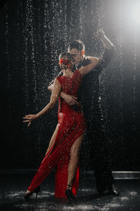 Rear view of shirtless man splashing water against black background