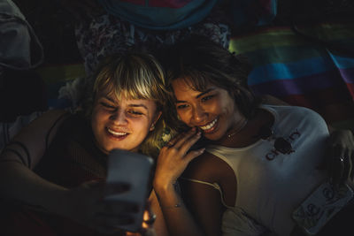 Happy non-binary person taking selfie with female friend through smart phone