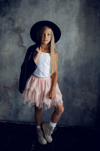 Fashionable girl model in a leather jacket skirt and shoes standing against the wall in the studio