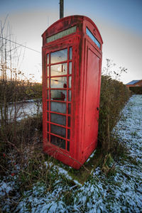Red telephone booth on field against sky