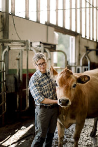 Mature female farmer standing with cow at cattle farm