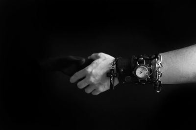 Cropped image of people holding hands against black background