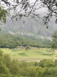 Scenic view of field by trees and houses against mountain