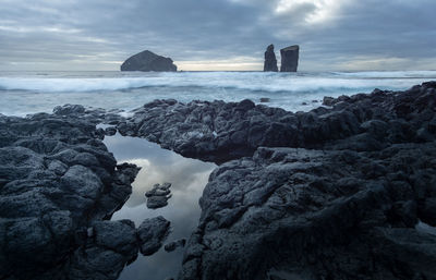 Rocks on beach against sky during sunset