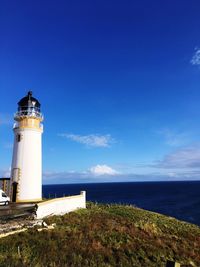 Lighthouse by sea against blue sky