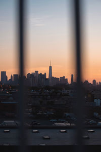 One world trade center in city against sky seen through fence during sunset