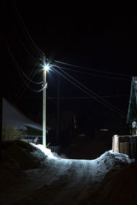 Illuminated street light on snow against sky at night