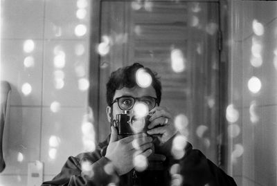 Portrait of man holding camera reflecting in mirror