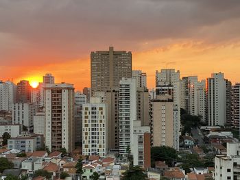Buildings in city against romantic sky at sunset