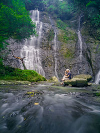 Rear view of man sitting against waterfall