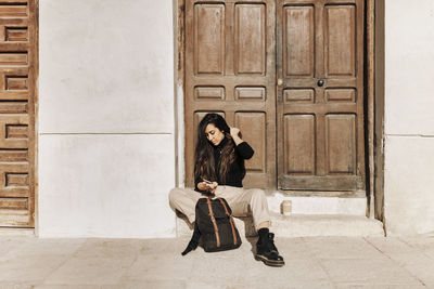 Full length portrait of woman sitting at entrance of building