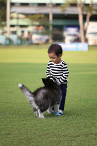 Full length of boy playing with dog on grass outdoors