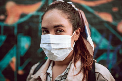 Portrait of a young woman with a mask agaisnt graffiti wall