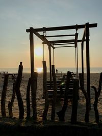 Silhouette wooden posts on beach against sky during sunset