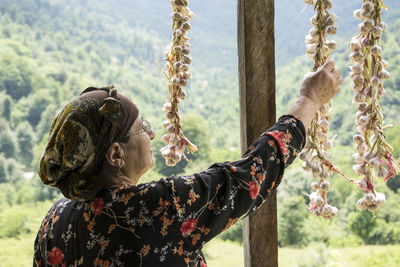 Rear view of woman hanging garlic cloves outdoors