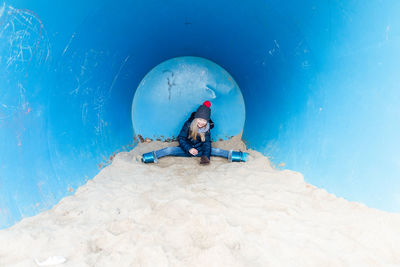 Full length of boy sitting by blue sea