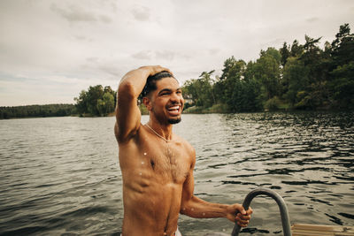 Happy shirtless man with head in hand enjoying swimming at lake during vacation