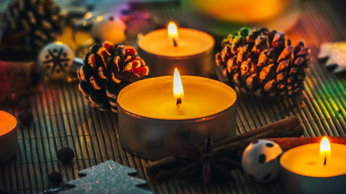 Close-up of burning tea lights amidst pine cones on table