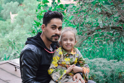 Portrait of man with cute girl sitting against plants