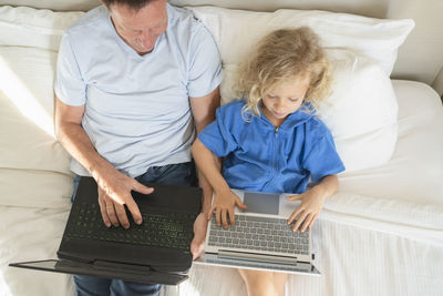 Girl and man using laptops on bed at home