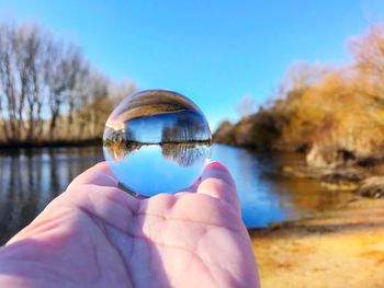 Close-up of hand holding crystal ball against trees