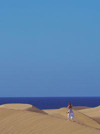 Woman walking on sand against sea and clear sky