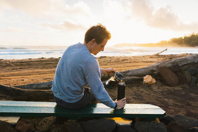 Man pouring coffee at sunrise on beach. 