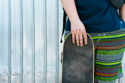 Midsection of man holding skateboard while standing against wall