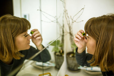 Close-up of woman applying mascara while reflecting in mirror at home
