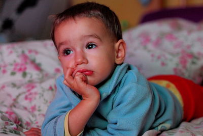 Cute thoughtful baby boy looking away while lying on bed