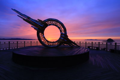 Illuminated pier over sea against sky during sunset