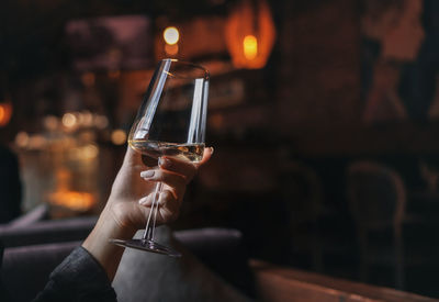 Female hand with french manicure holding a glass with wine on naturally blurred background