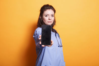 Portrait of young woman holding smart phone against yellow background