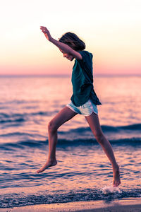 Full length of girl jumping on beach against sky during sunset