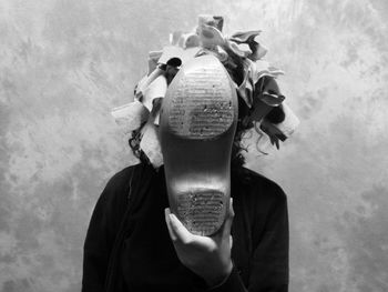 Woman hiding face with shoe against wall