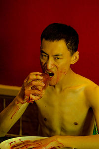 Portrait of shirtless angry man eating raw meat at home