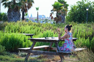 Woman using phone while sitting on seat by plants