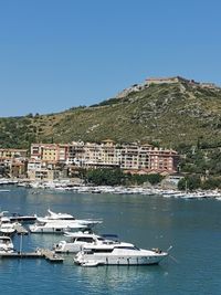 Sailboats in sea by townscape against clear blue sky