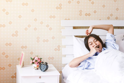 Young woman yawning while lying on bed at home