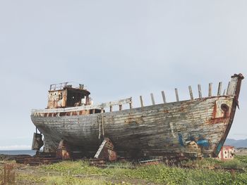 Old abandoned boat on field by sea against clear sky