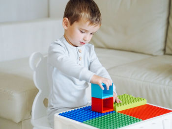 Cute toddler 3 years boy in grey pajamas playoing lego constructor in bright interior