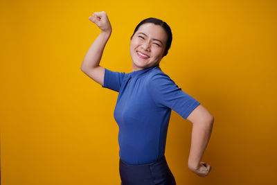 Smiling young woman standing against yellow background
