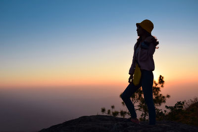 Side view of woman standing against sky during sunset